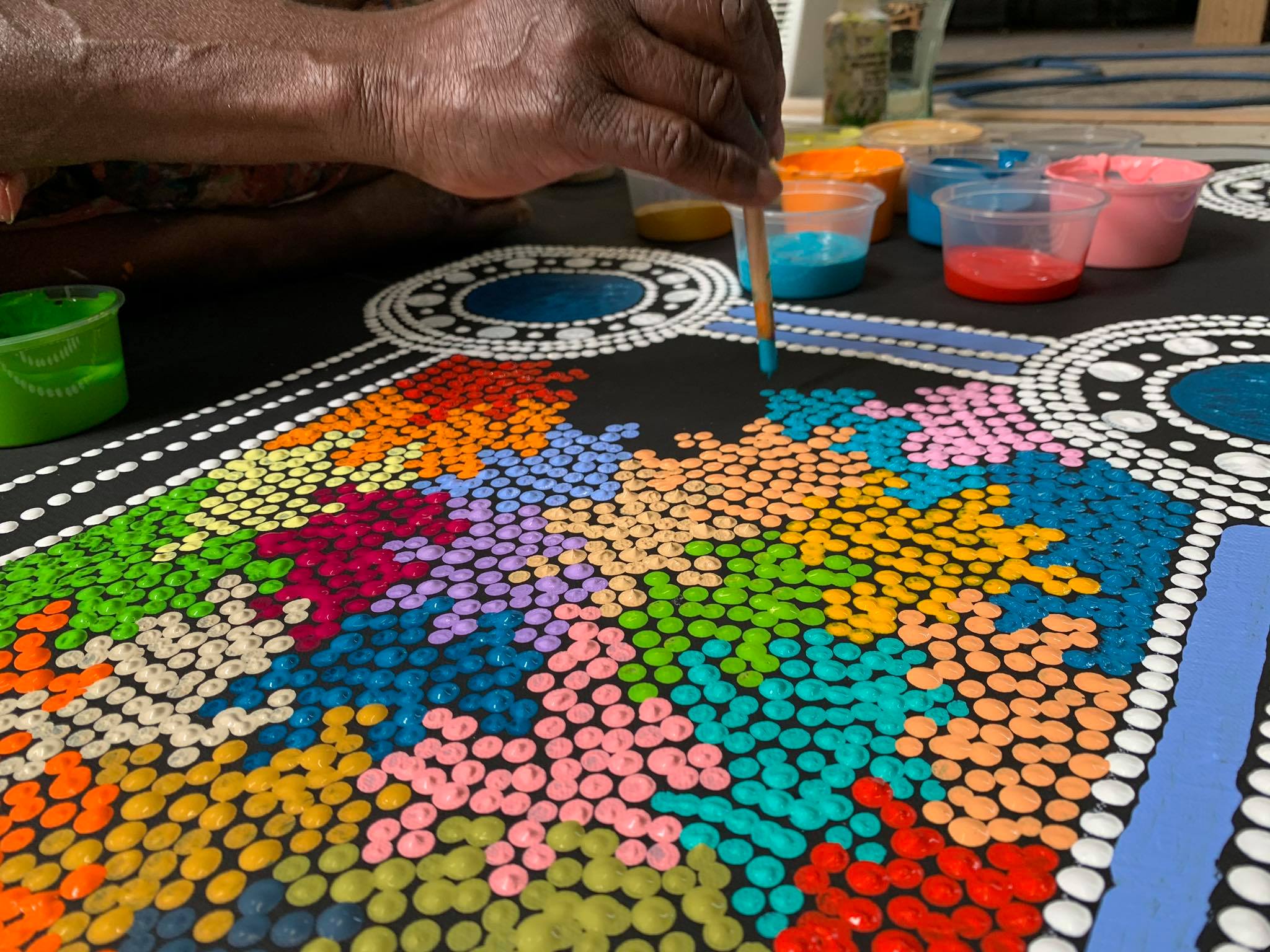 Woman's hand painting colourful dots on black canvas | Raintree Art Aboriginal Art Ballarat
