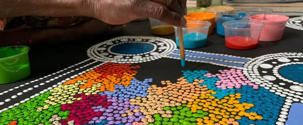 Woman's hand painting colourful dots on black canvas | Raintree Art Aboriginal Art Ballarat