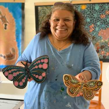 Aboriginal Artist Deidre Burgoyne Rosier holding two hand-painted butterflies at Raintree Art, Aboriginal Art Ballarat